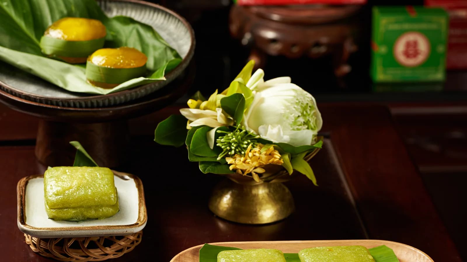 Các đĩa bánh trên bàn gỗ, bên bình hoa trắng và hộp quà